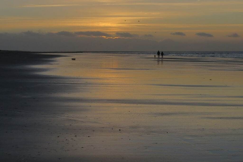 A beach scene with a sunset, calm water, and a few people walking.