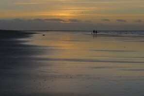 A beach scene with a sunset, calm water, and a few people walking. - Apartment 2 in the Mare Cimbria building (Norddorf auf Amrum)