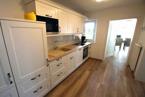 A kitchen with white cabinets, a microwave, a sink, and a window. - Apartment 2 in the Mare Cimbria building (Norddorf auf Amrum)