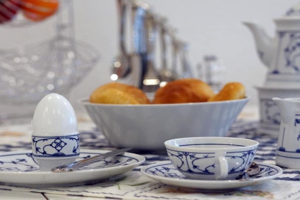 A table set with a teapot, a cup, a saucer, a bowl of bread, and a spoon.