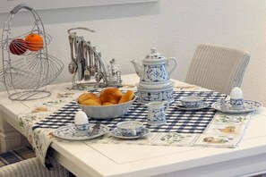 Une table à manger dressée avec une nappe à carreaux, une théière, des tasses et un panier de fruits.