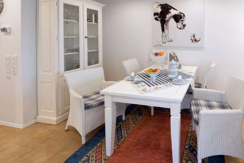 A dining area with a white table, wicker chairs, a patterned rug, and a cabinet with glass doors.