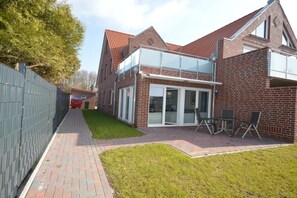 A two-story brick house with a glass balcony and a paved patio area. - Holiday apartment with 1 bedroom (Norden)
