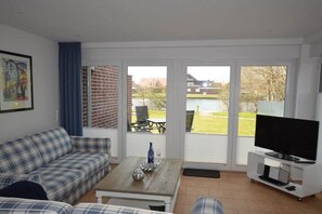 Ein Wohnzimmer mit Sofa, Couchtisch und TV-Möbel, große Fenster mit Blick auf einen Innenhof und Gebäude.