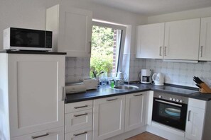 Une cuisine avec des meubles blancs, un four à micro-ondes, une machine à café et un grille-pain.