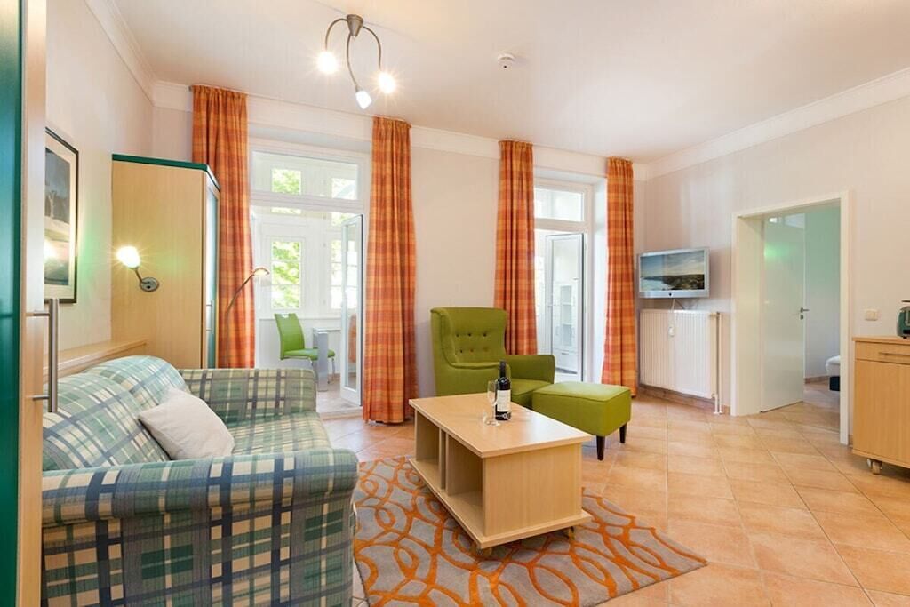 A furnished living room with a sofa, a green armchair, a wooden coffee table, and a patterned rug.