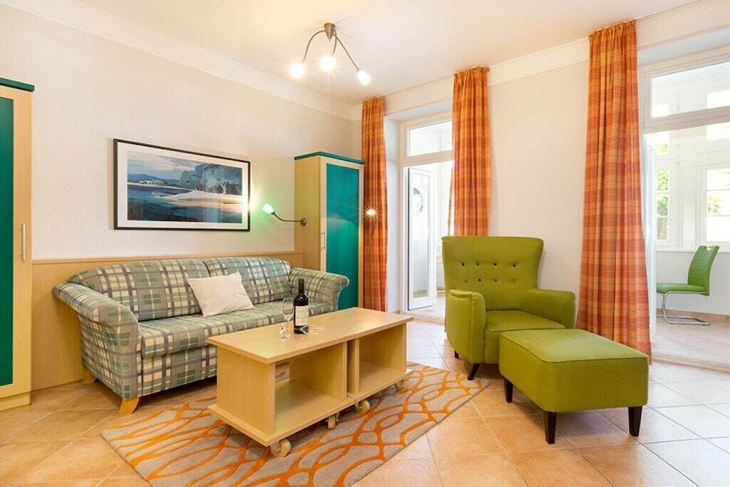 Un salon meublé comprenant un canapé, un fauteuil vert, une table basse et un tableau accroché au mur.