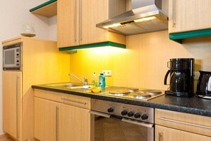 Een kleine keuken met een magnetron, kookplaat en koffiezetapparaat.