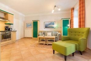 Een compacte leefruimte met een kitchenette, een bank, een groene fauteuil en een eettafel.