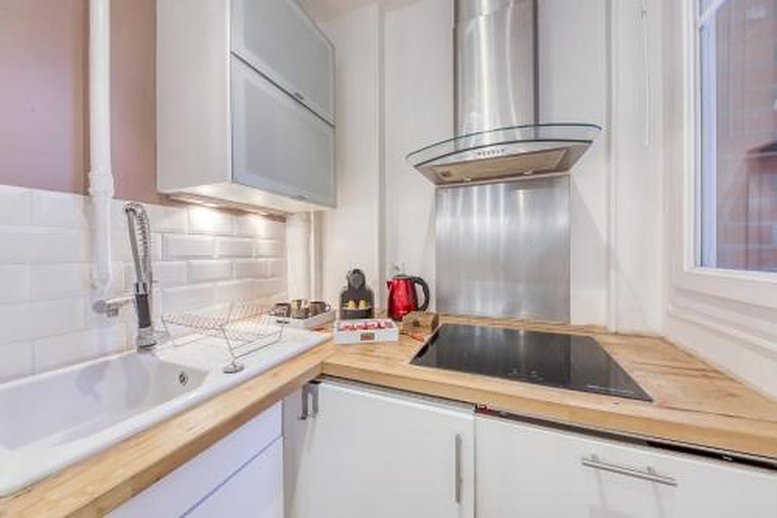 Una cocina moderna con gabinetes blancos, una campana extractora de acero inoxidable, una estufa integrada y un ventanal que proporciona luz natural.