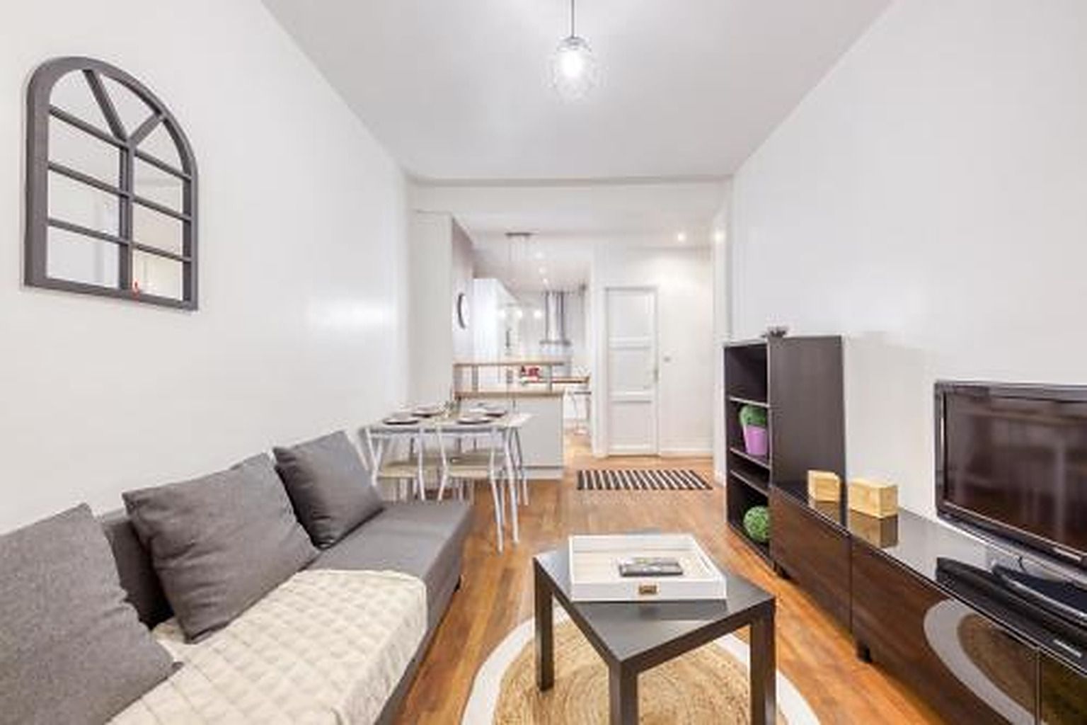 A modern living room with a sofa, coffee table, TV, and a dining area with chairs and a table.