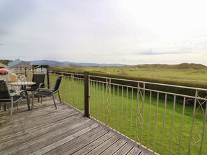 A wooden deck with outdoor seating, overlooking a grassy field and distant hills. - Ty'r Heulwen (Aberdovey)