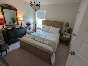 Quarto com cama, penteadeira, cadeira, abajur e janela.