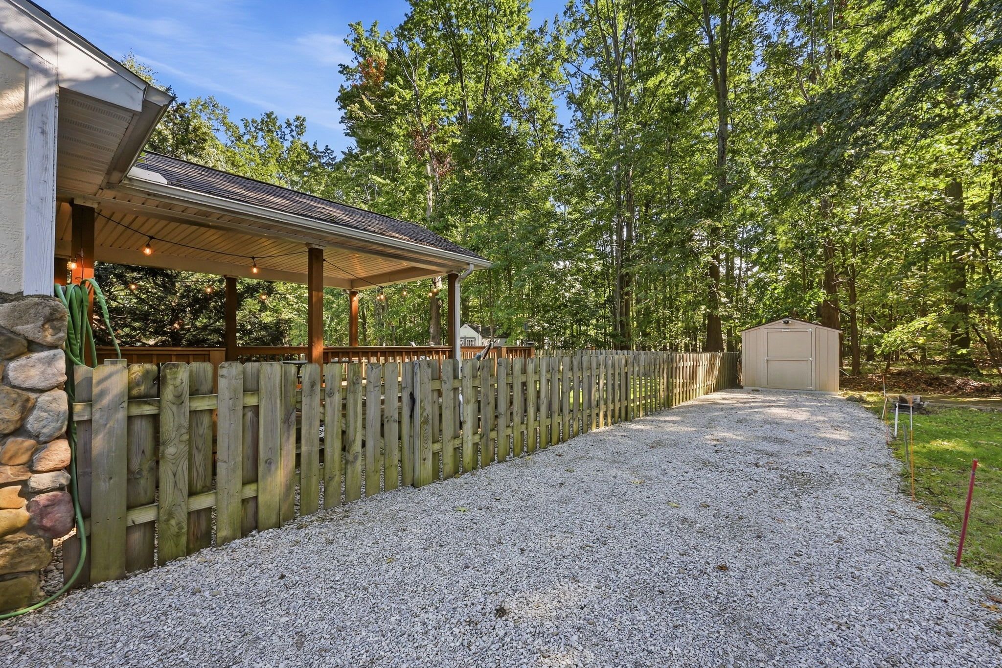 Un espace extérieur abrité avec des sièges, accessible par un chemin de gravier qui mène à une clôture en bois et à un abri de jardin.