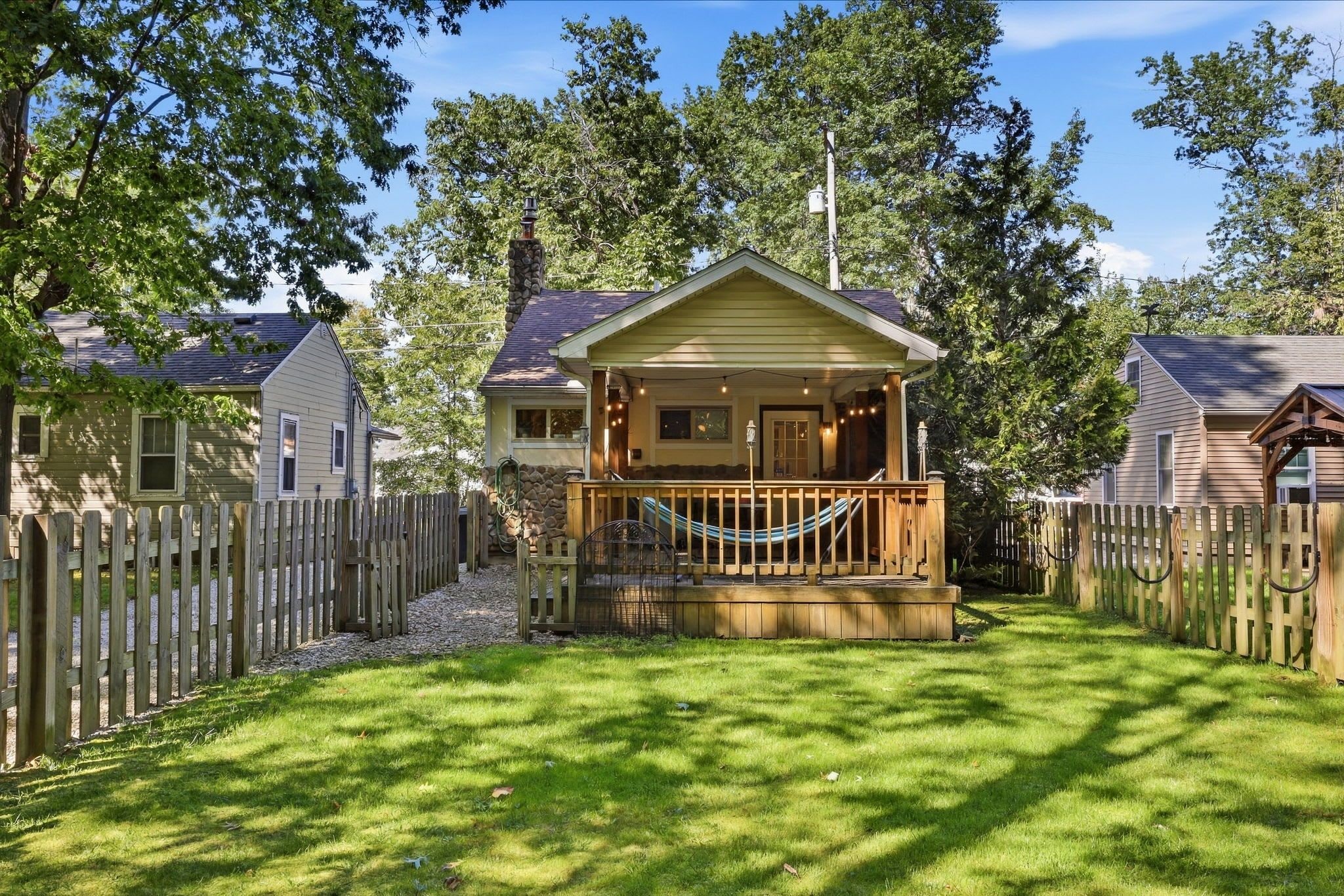 A small, single-story house with a porch, surrounded by a wooden fence and a grassy yard.