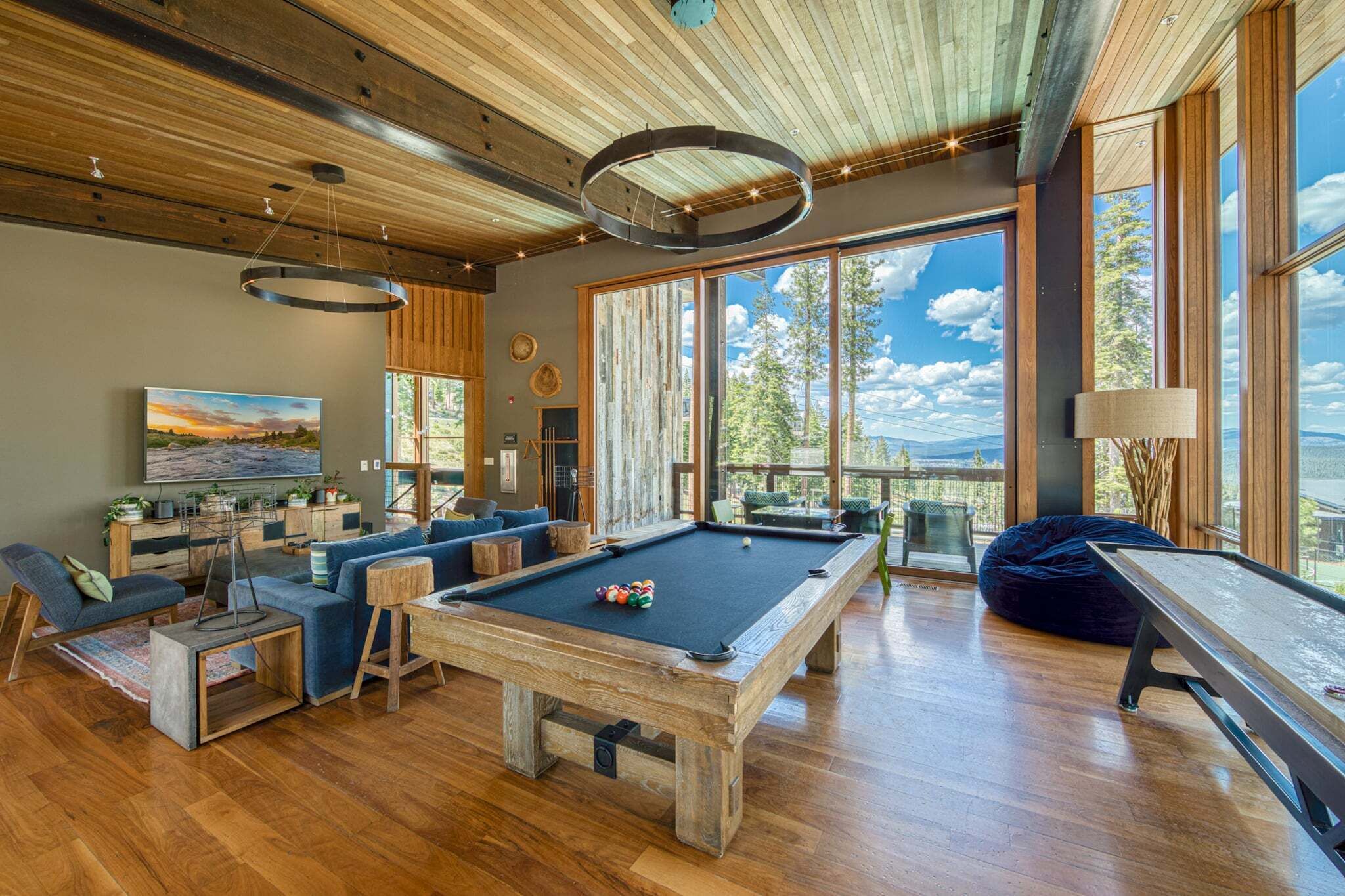 Un salon moderne doté d’une table de billard, de sièges confortables et de grandes fenêtres offrant une vue sur l’extérieur.