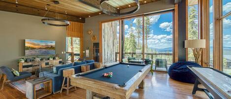 Un salon moderne doté d’une table de billard, de sièges confortables et de grandes fenêtres offrant une vue sur l’extérieur.