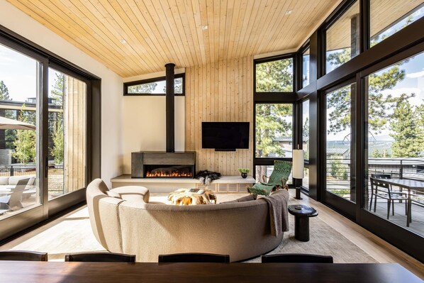 A modern living room with a fireplace, comfortable seating, and large windows offering a view of the outdoors. - Site Line Ski-In/Ski-Out at Northstar by Tahoe Getaways - Pet-Friendly 4BR w Hot Tub & HOA (Truckee)