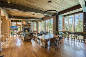 A spacious indoor area with a large wooden dining table, comfortable seating, and large windows offering a view of the outdoors. - Site Line Ski-In/Ski-Out at Northstar by Tahoe Getaways - Pet-Friendly 4BR w Hot Tub & HOA (Truckee)