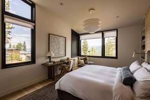 Ein Schlafzimmer mit einem großen Bett, einem Schreibtisch und zwei Fenstern mit Blick auf Bäume und Berge.