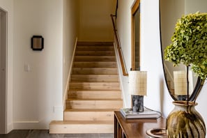 A wooden staircase leading to a second floor, a wall-mounted light fixture, and a decorative plant in a vase. - Site Line Ski-In/Ski-Out at Northstar by Tahoe Getaways - Pet-Friendly 4BR w Hot Tub & HOA (Truckee)