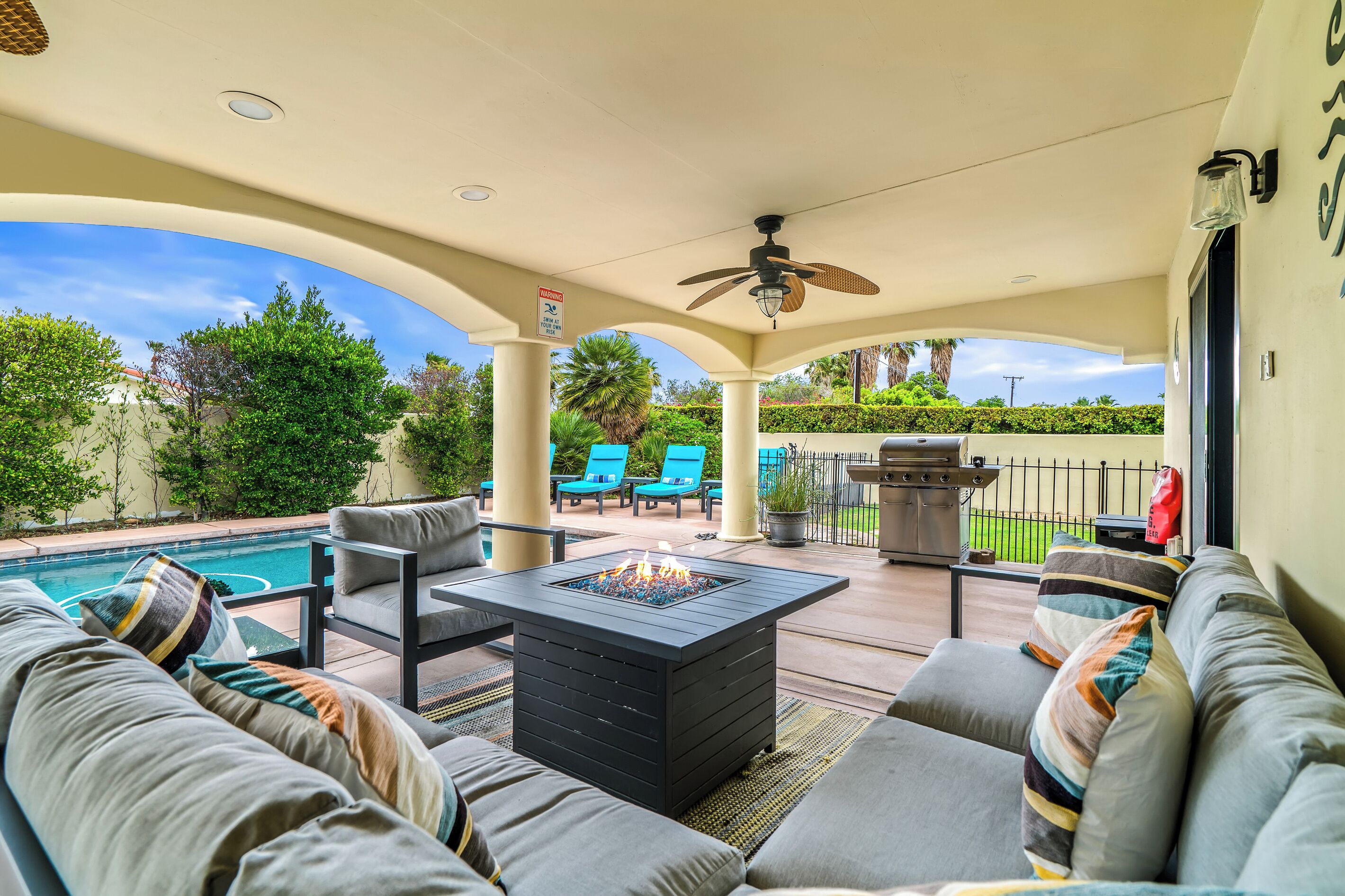An outdoor patio with a pool, seating area, and a ceiling fan.