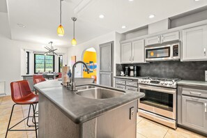 A modern kitchen with a central island, stainless steel appliances, and a dining area with red chairs. - Pet Friendly Desert Escape with Private Pool, Spa & Mountain View City id 069584 (Palm Springs)