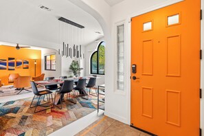 Ein modernes Interieur mit Essbereich, einer leuchtend orangefarbenen Tür und Blick ins Freie.