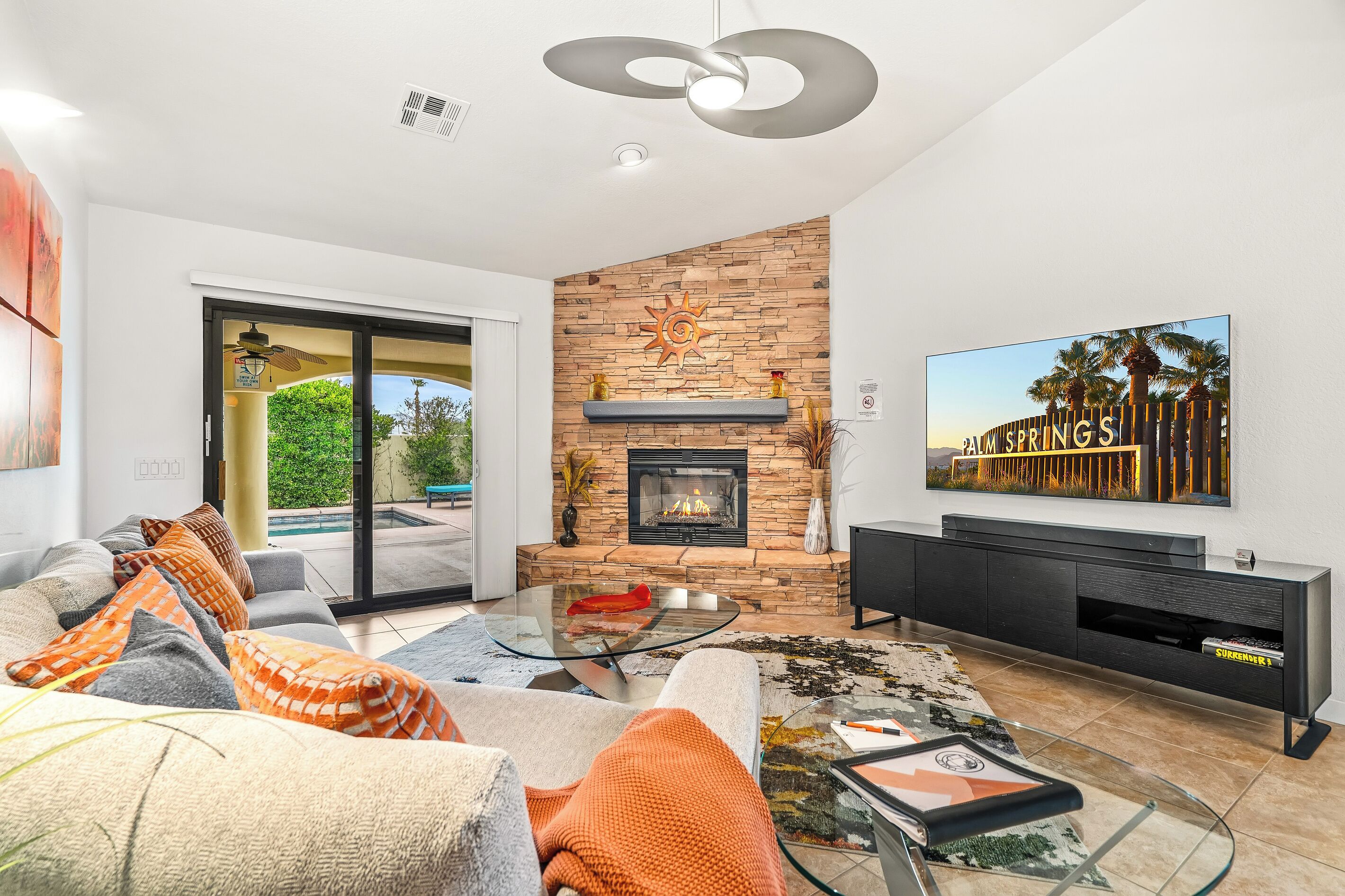 A modern living room with a fireplace, a glass coffee table, and a flat-screen TV mounted on the wall.