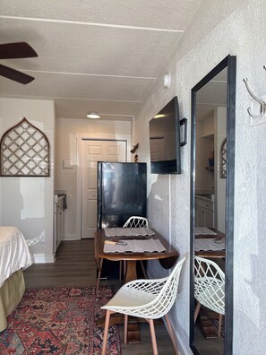 Habitación pequeña con cama, un escritorio con silla, un espejo y un tapete estampado.