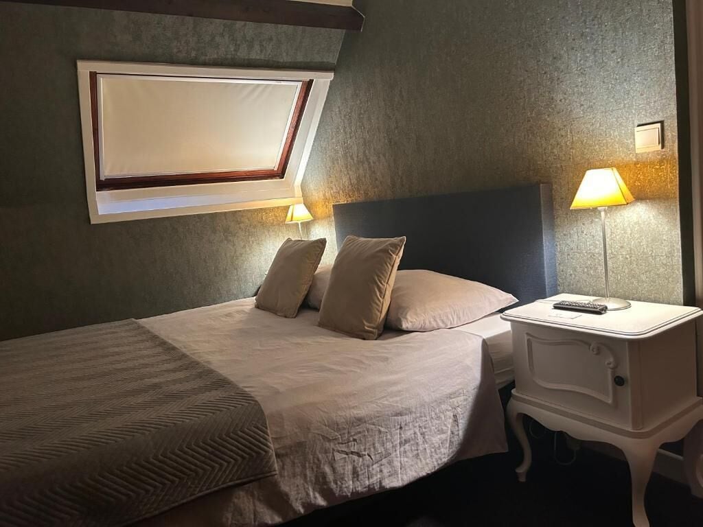 Quarto de hotel com cama, abajures, mesa de cabeceira e janela com vista.