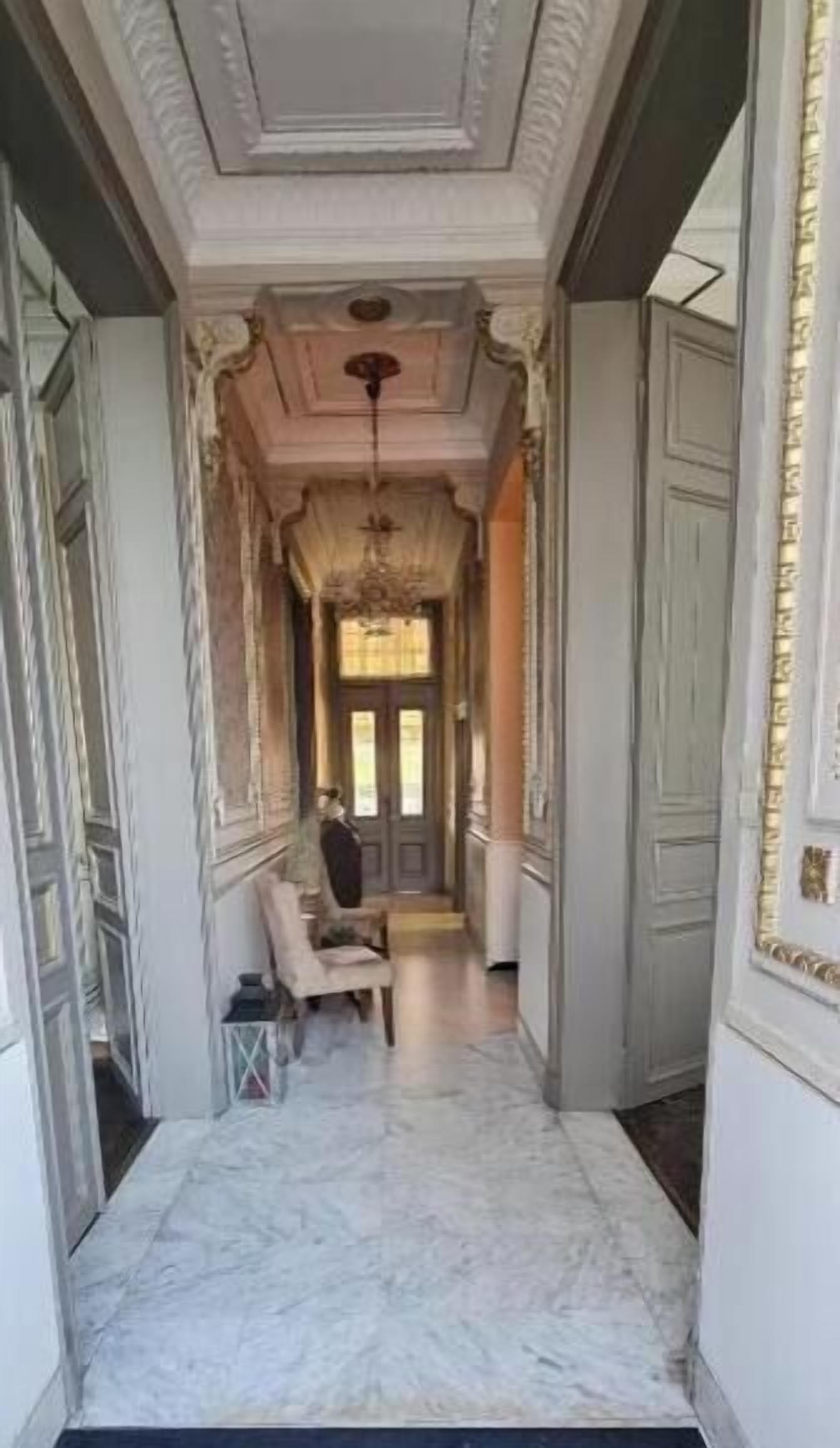 A hallway with a marble floor, a chandelier, and a door at the end.