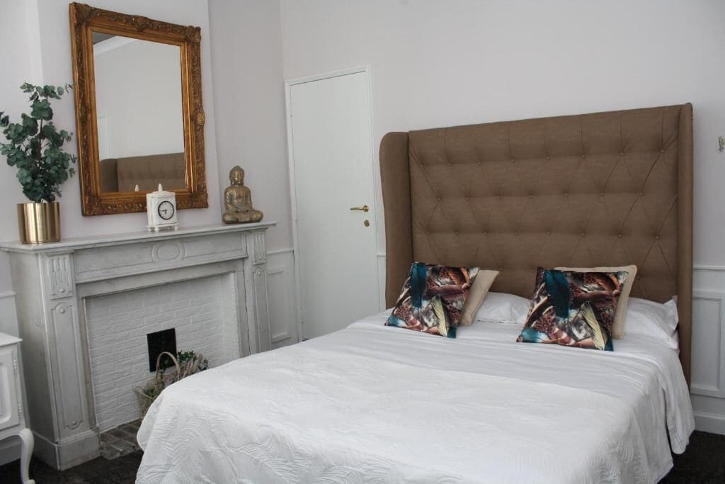 Une chambre à coucher avec un grand lit, une cheminée, un miroir et une porte.