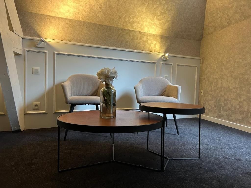 A room with two armchairs and a round table, a vase with flowers, and a textured wall.