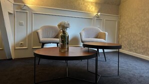 Una habitación con dos sillones, una mesa redonda, un jarrón con flores y una pared con textura.