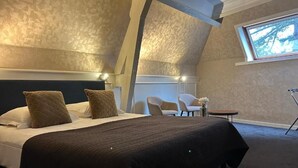A bedroom with a large bed, two chairs, a small table, and a window with a view. - Hotel Vredehof (Damme)