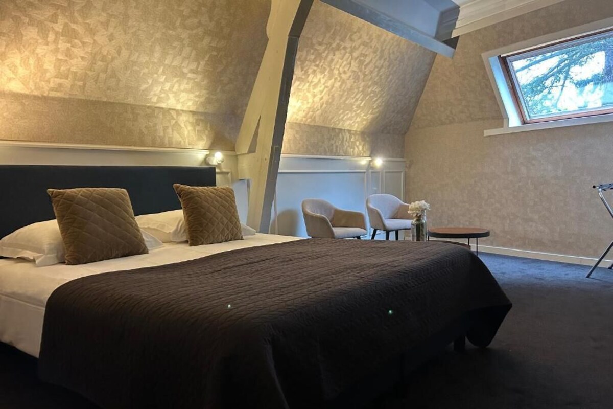 Une chambre à coucher avec un grand lit, deux chaises, une petite table et une fenêtre donnant sur un beau paysage.