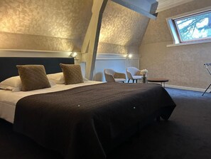 Une chambre à coucher avec un grand lit, deux chaises, une petite table et une fenêtre donnant sur un beau paysage.