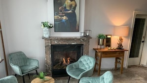 Una habitación con chimenea, dos sillones tapizados, una mesita redonda y un cuadro sobre la repisa.