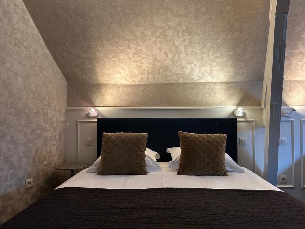 Habitación de hotel con cama, dos almohadas, cabecera con luces y pared con textura.