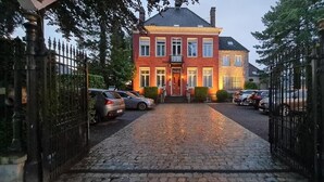 A red brick building with a cobblestone driveway and a gated entrance. - Hotel Vredehof (Damme)