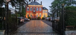 Un bâtiment en briques rouges, avec une allée pavée et une entrée fermée par un portail.
