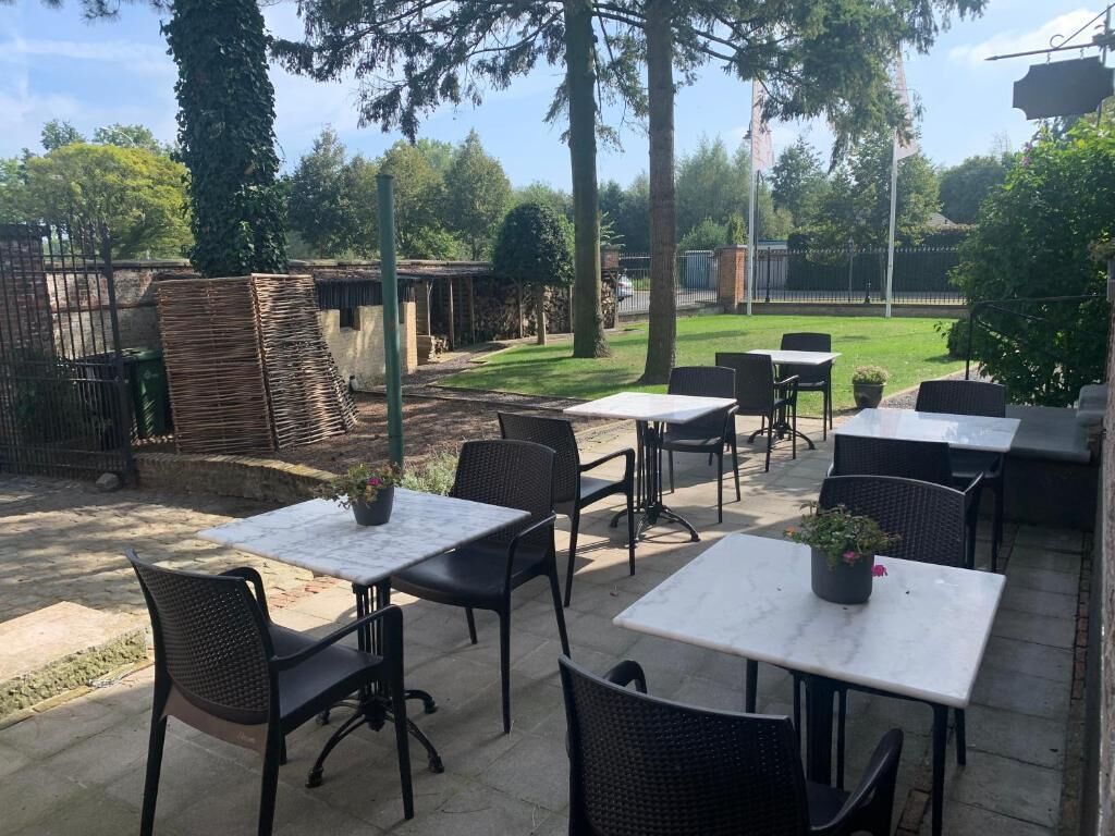 An outdoor patio area with tables and chairs, surrounded by trees and a fence.