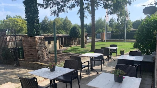 An outdoor patio area with tables and chairs, surrounded by trees and a fence. - Hotel Vredehof (Damme)
