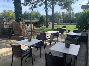 Un patio al aire libre con mesas y sillas, rodeado de árboles y una valla.