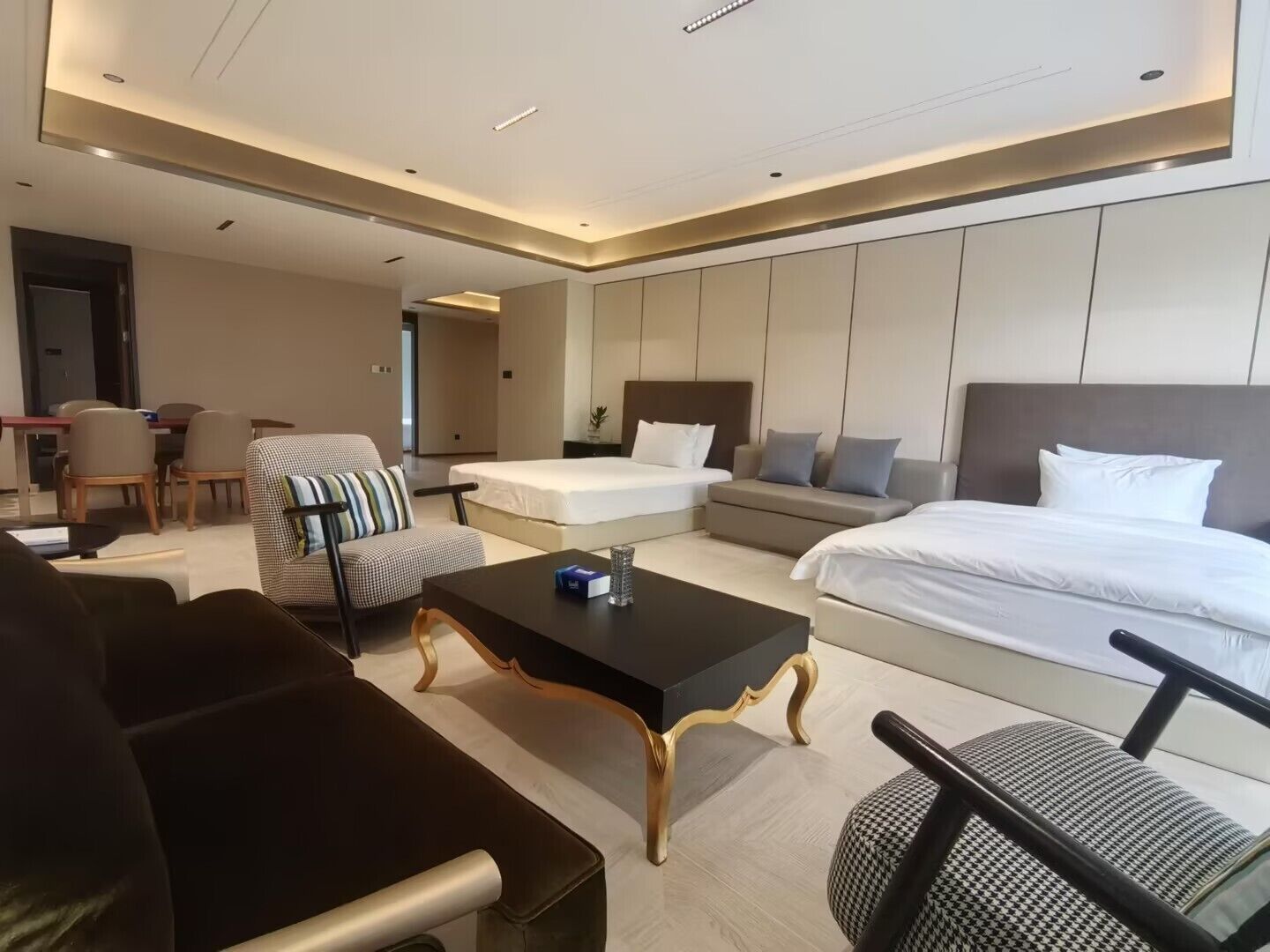 Una habitación de hotel moderna con una cama grande, un sofá, una mesa de comedor y una zona de estar separada.