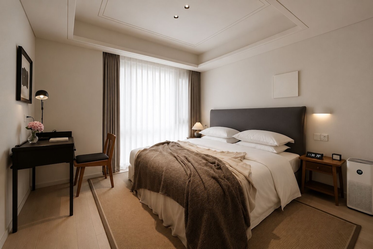 Ett hotellrum med en säng, ett nattduksbord, en lampa, en stol, ett skrivbord och ett fönster med gardiner.