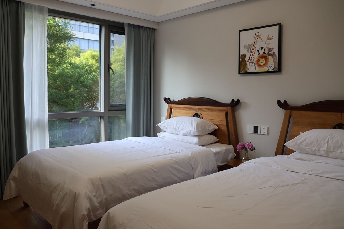 Ett hotellrum med två sängar, ett fönster med gardiner, ett konstverk som hänger på väggen och en vas med blommor.