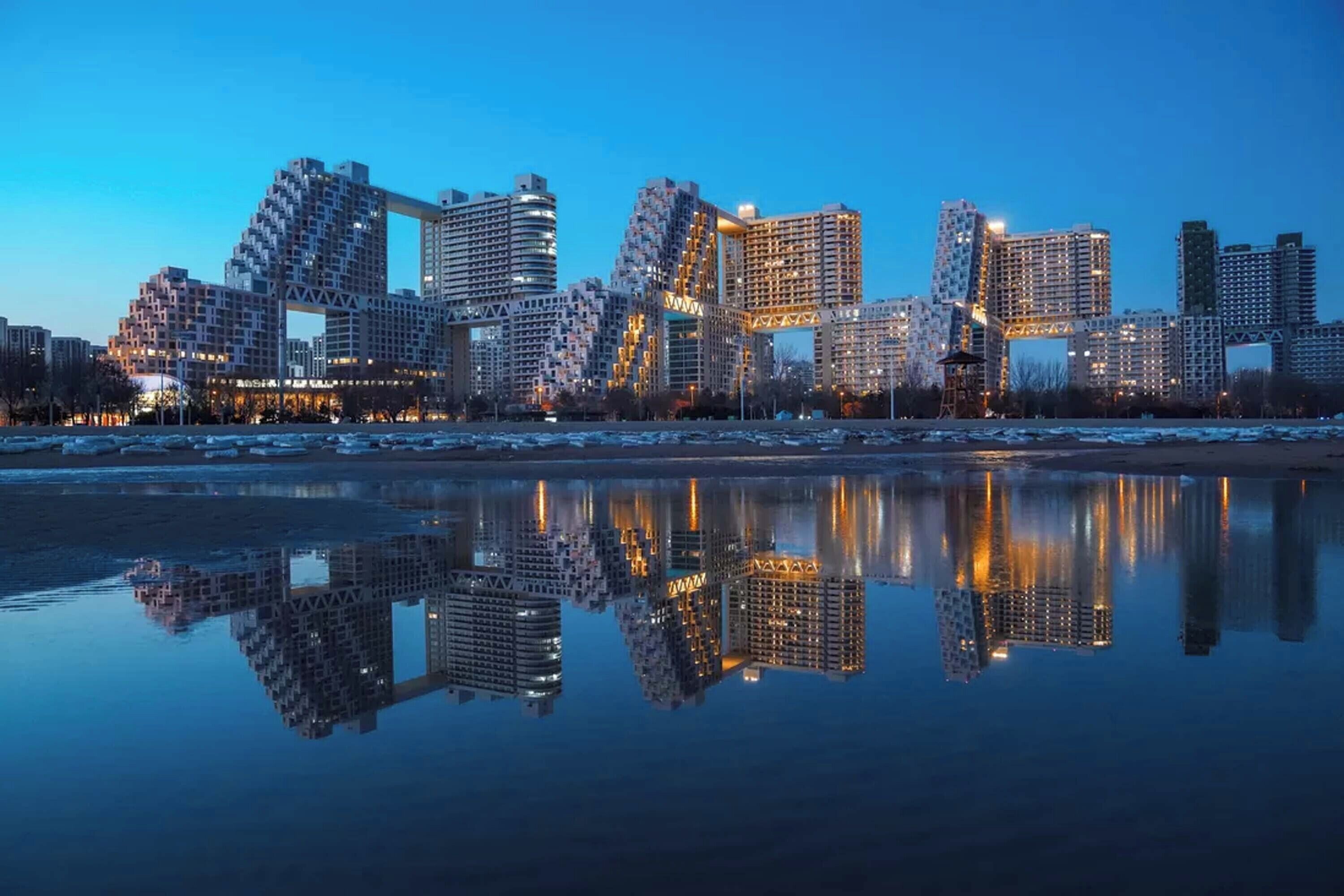 Un horizonte urbano con arquitectura moderna reflejado en aguas tranquilas.