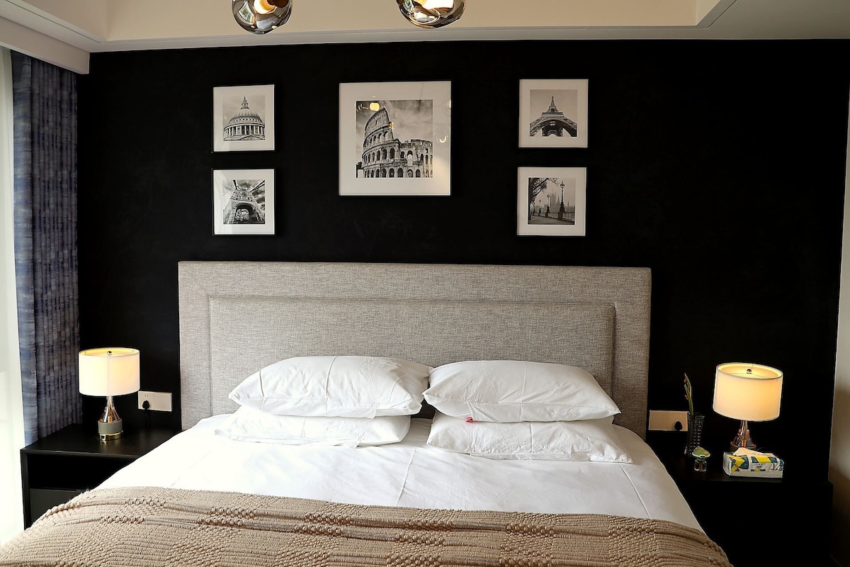 Ett hotellrum med en stor säng, två sänglampor och fyra inramade tavlor på väggen.